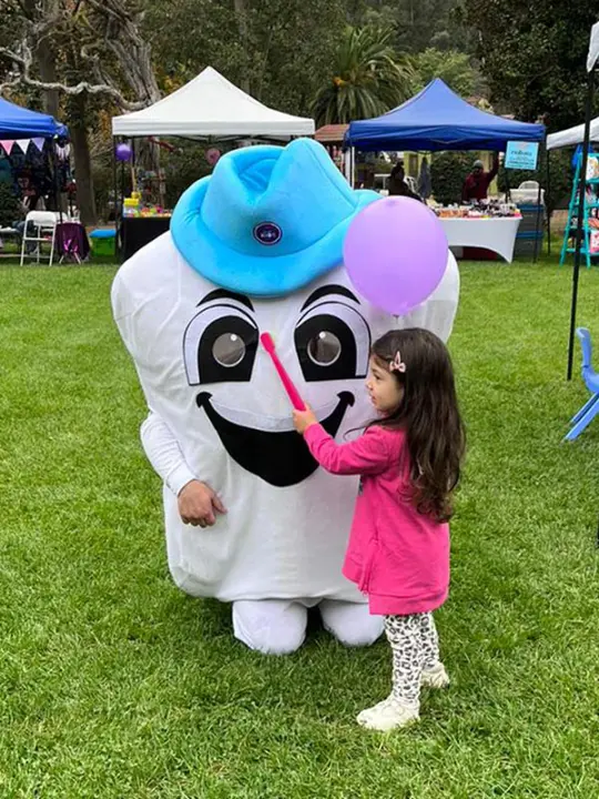 Mascota de Dentosalud con una niña en una feria de salud